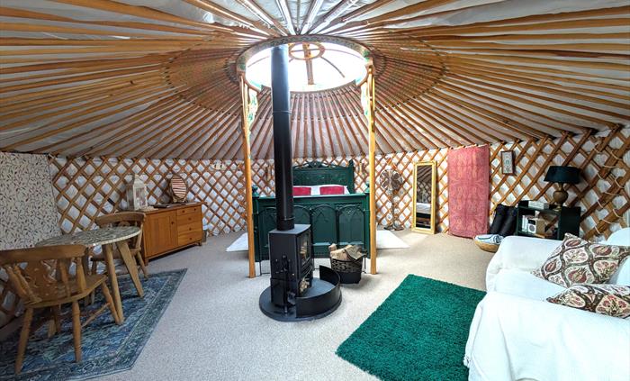 The yurt is round with many painted wood rafters radiating from the central roof light. There is a central logburner on a round slate hearth. At the b